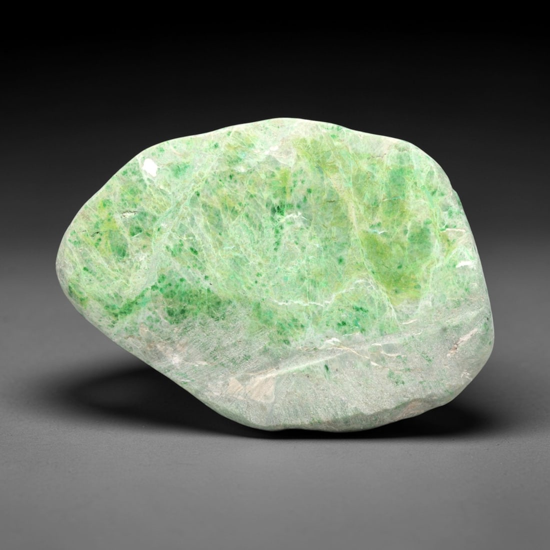 A Burmese Jadeite Jade Rough, 20th Century, 61FS: A piece of Burmese jadeite jade rough, with a pale greenish-white matrix and vibrant green mineral inclusions. The rough is shaped as an irregular, flattened form, with visible natural fractures and a