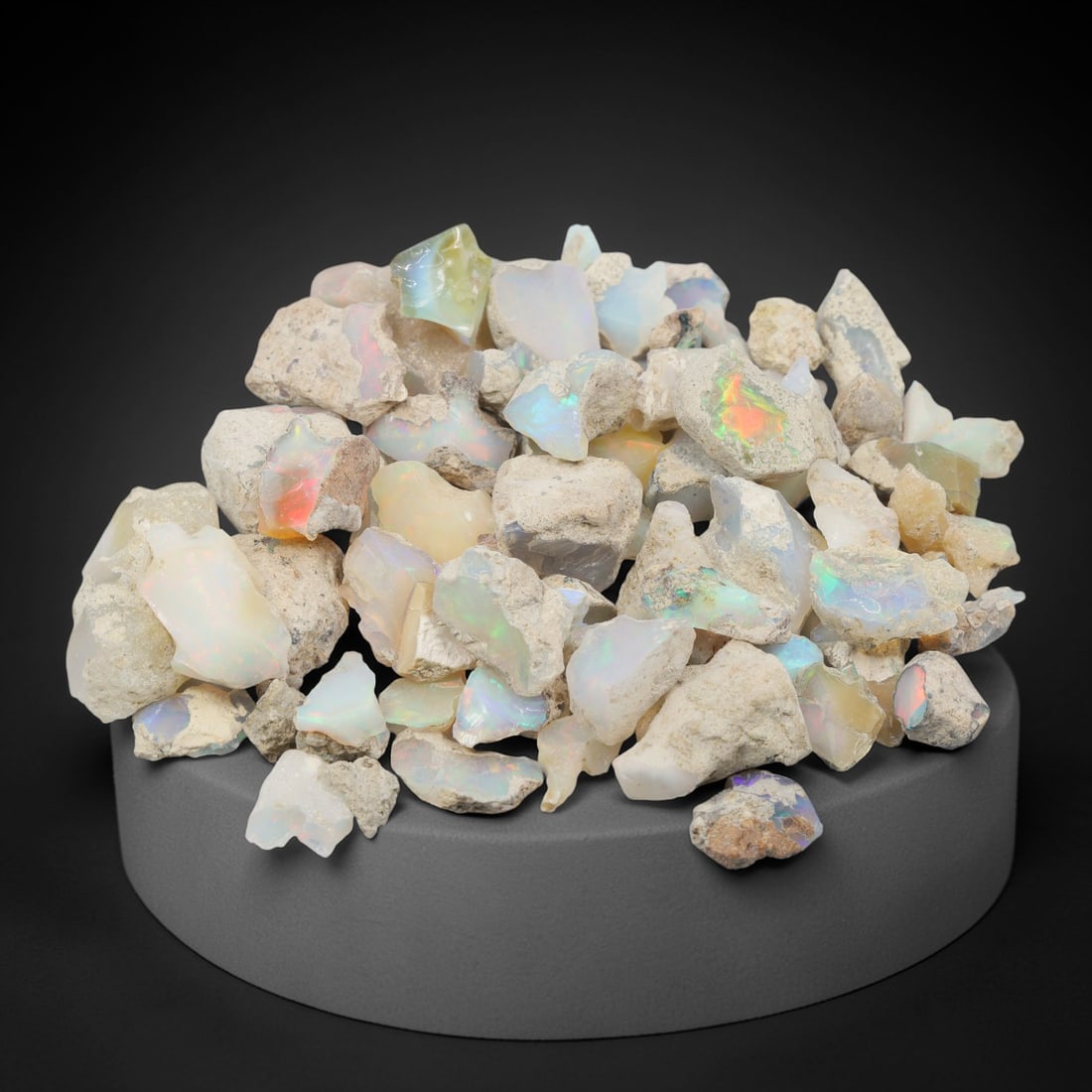 An Ethiopian Welo Opal Rough Lot, 54.72g, 57ZH: A parcel of rough Welo opal, with individual pieces ranging from 1-2.7 cm in size. The specimens exhibit a milky to translucent base, with visible play-of-color displaying flashes of blue, green, yell