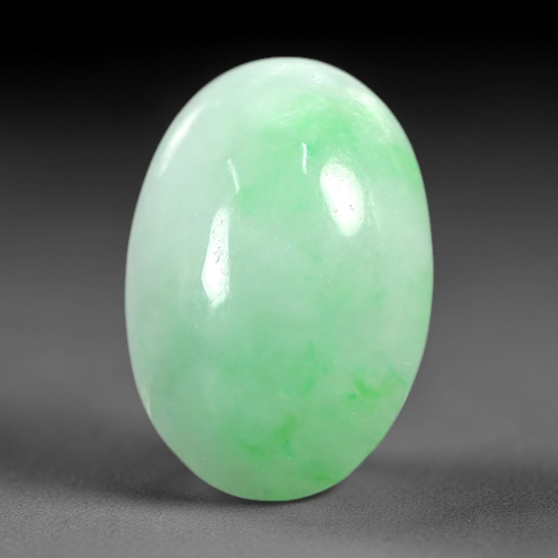 4.64 Carats Apple Green Burmese Jadeite Jade Cabochon - Natural Loose Gemstone, 63AC: This oval Burmese jadeite jade cabochon exhibits a soft apple green hue, with concentrated patches of richer green that add depth and dimension to its milky translucency. The smooth, domed cabochon cu