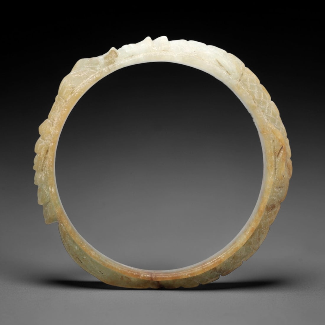 A Chinese Jadeite Jade Bangle Bracelet, 20th Century, 43FS: Carved from pale celadon jadeite jade with natural russet and yellowish inclusions, the bangle is formed as a continuous circular band. The exterior surface is decorated with raised relief carving dep