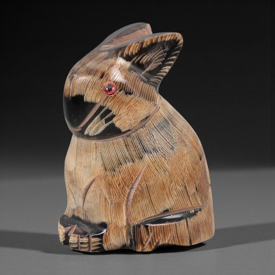 An East Asian Ox Horn Rabbit Effigy, 20th Century, 7FJ: Carved from a single section of ox horn with visible natural striations and tonal variation ranging from pale honey to deep brown, the object is formed as a seated rabbit rendered in the round. The he