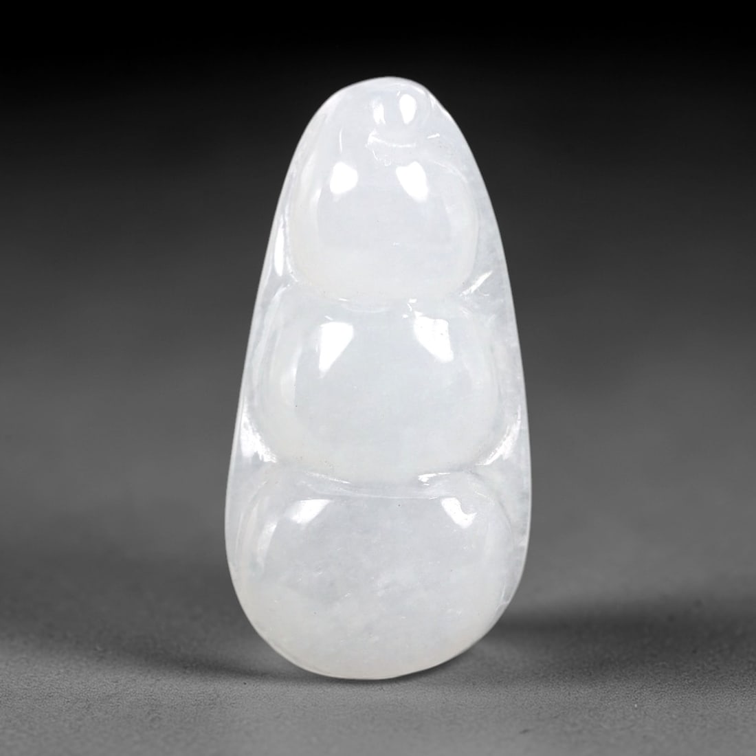 A Chinese Icy Jadeite Jade Bean Pendant, 20th Century, 59AB: Carved from translucent icy jadeite with a pale milky-white hue and minor natural inclusions, the pendant is shaped as a stylized three-segmented bean pod. Smooth, rounded contours define each segment