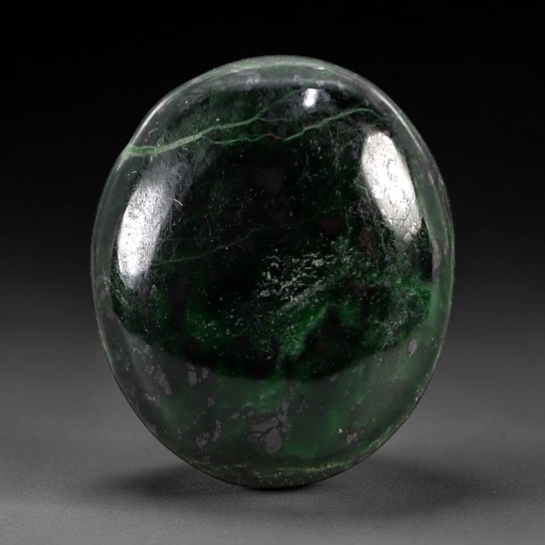 6.94 Carats Deep Green Maw Sit Sit Jade Cabochon - Natural Burmese Stone, 12AB: This maw sit sit jade cabochon is fashioned into an oval, domed form with a highly polished surface. The material exhibits a deep, saturated green matrix, interspersed with distinct, darker green and