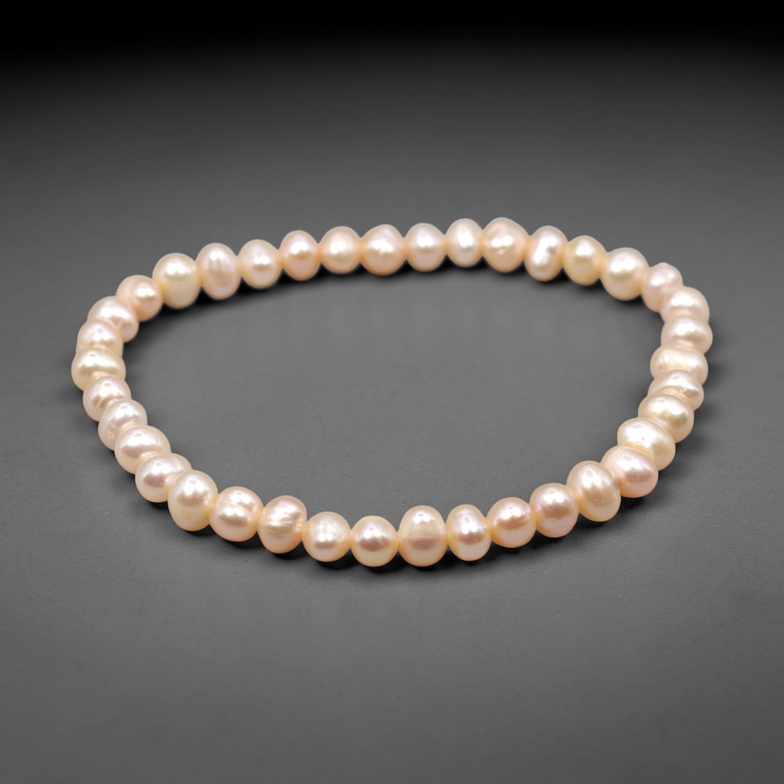 A Cultured Pearl Bracelet, 20th Century, 92ZH: Composed of a single strand of cultured pearls, each with a soft pinkish-white hue and natural, slightly irregular baroque shape. The pearls exhibit a lustrous, iridescent surface with subtle nacre, s