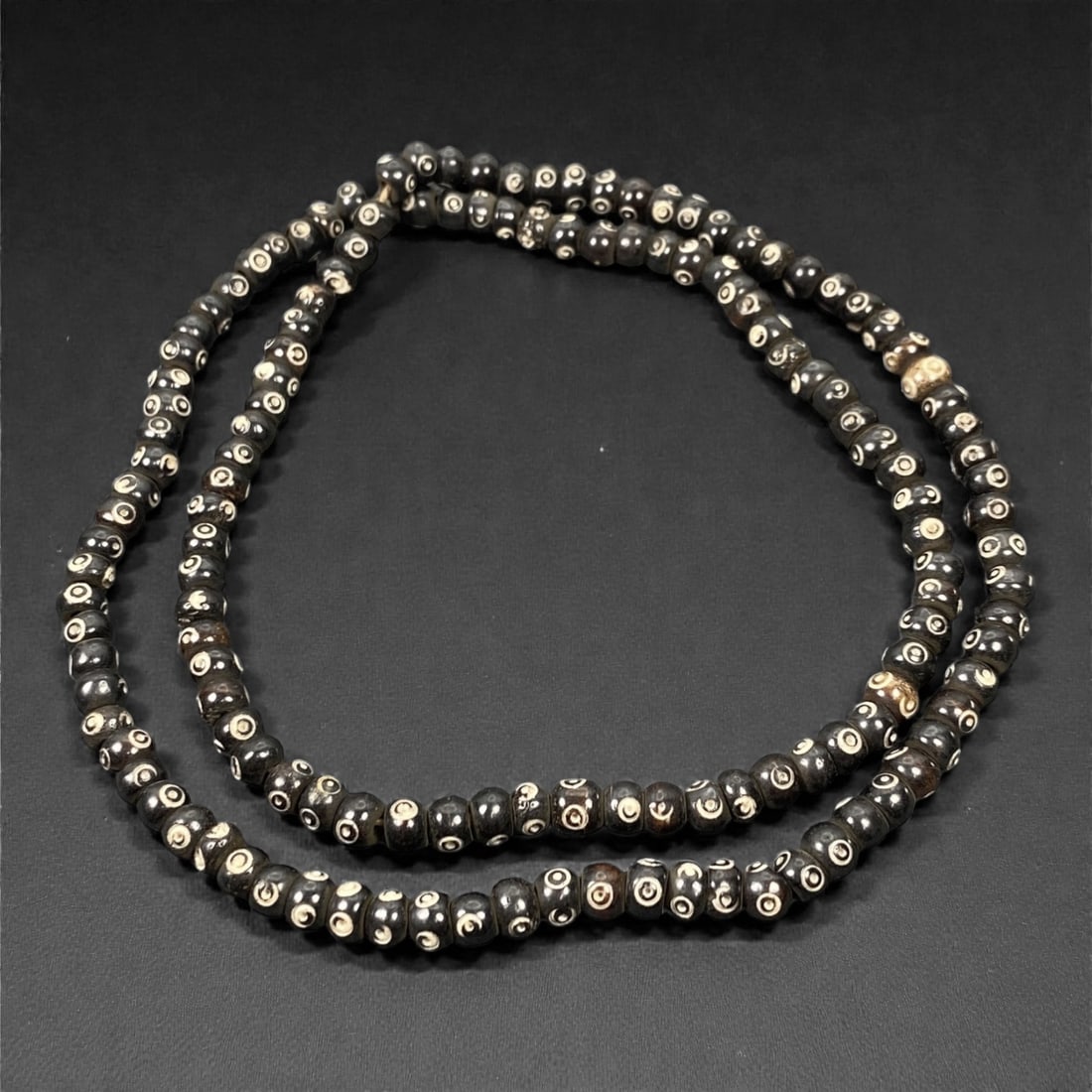 A Single Strand of Tibetan Bone Beads with Concentric Circle (Dzi-Eye) Motif, 20th Century, 88S: A complete, wearable single strand of Tibetan bone prayer beads, measuring 33 cm (13 in.) in total length. The strand is meticulously composed of small, uniformly sized spherical bone beads, each intr