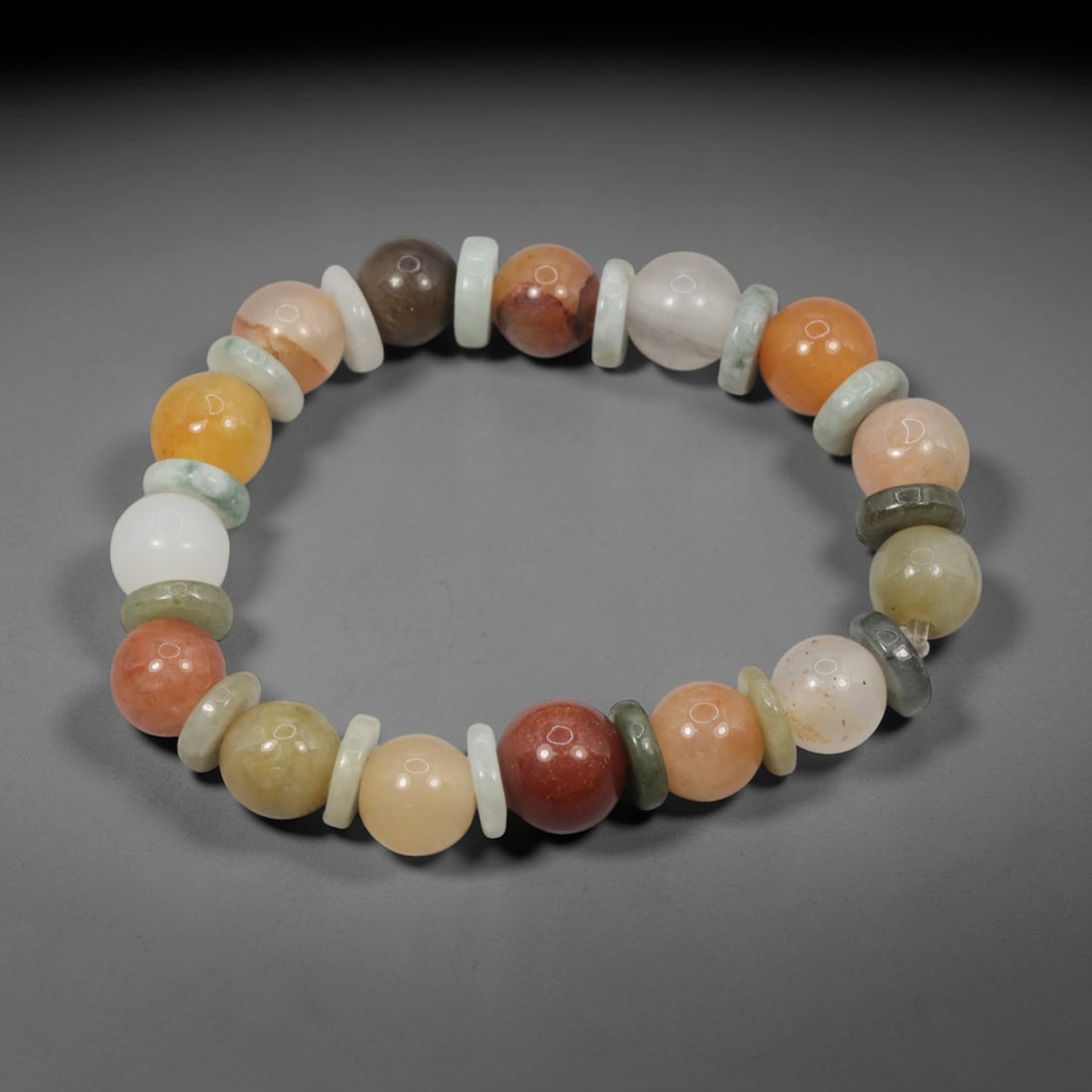 A Chinese Quartz and Jadeite Jade Bead Bracelet, 20th Century, 47ZK: Strung with spherical beads of quartz and jadeite jade, separated by flat disc-shaped spacers. The quartz beads display a spectrum of natural hues, including white, pale yellow, orange, peach, reddish