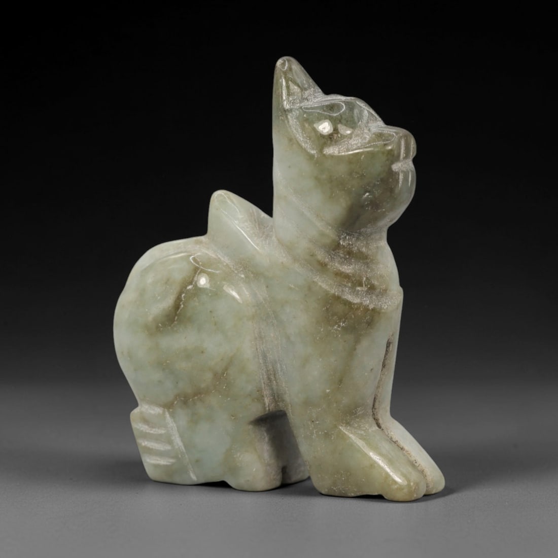 A Chinese Jadeite Jade Animal Figure, 20th Century, 13ZL: Carved from pale green jadeite with natural greyish-brown inclusions, the object is formed as a seated animal figure, likely a stylized cat or mythical beast. The figure is depicted with upright