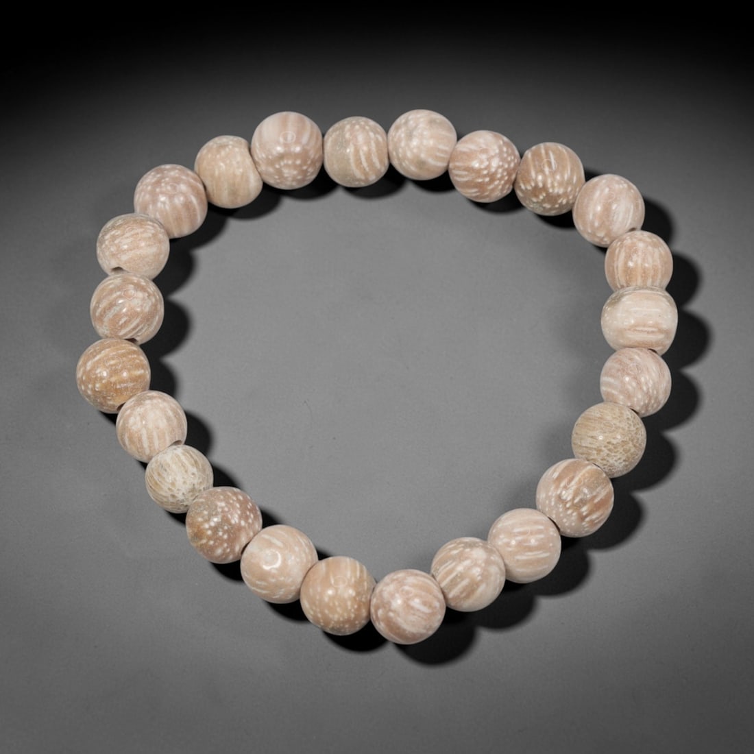 A Chinese Fossilised Wood Bead Bracelet, 20th Century, 50ZK: Composed of a single strand of spherical fossilised wood beads forming a circular bracelet. The beads exhibit natural tonal variation from pale beige to light brown, with distinct linear and spotted o
