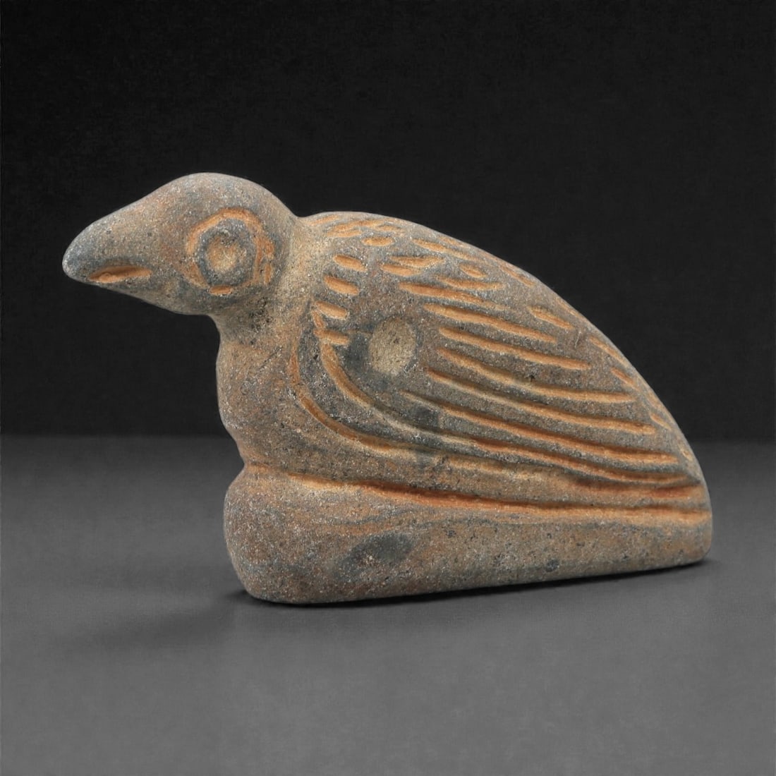 An Ancient Near Eastern Stone Vulture Effigy, 2nd-1st Millennium BCE, 33FL: Carved from gray stone with orange-brown incised patina, the object depicts a vulture in a crouched posture. The head features a prominent beak and a circular eye, while the body is decorated with inc