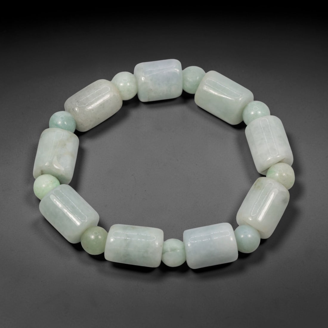 A Chinese Jadeite Jade Bead Bracelet, 20th Century, 26ZK: Composed of a single strand of barrel-shaped and spherical jadeite jade beads forming a circular bracelet. The barrel-shaped beads display natural tonal variation from pale green to light green, with
