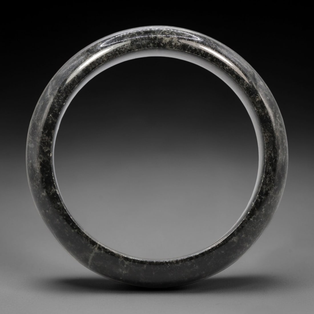 A Black Jadeite Bangle, 20th Century, 25XM: Carved from black jadeite, this bangle is formed as a continuous circular band with a rounded, slightly thickened profile. The material exhibits a deep, uniform black bodycolor with subtle greyish-whi