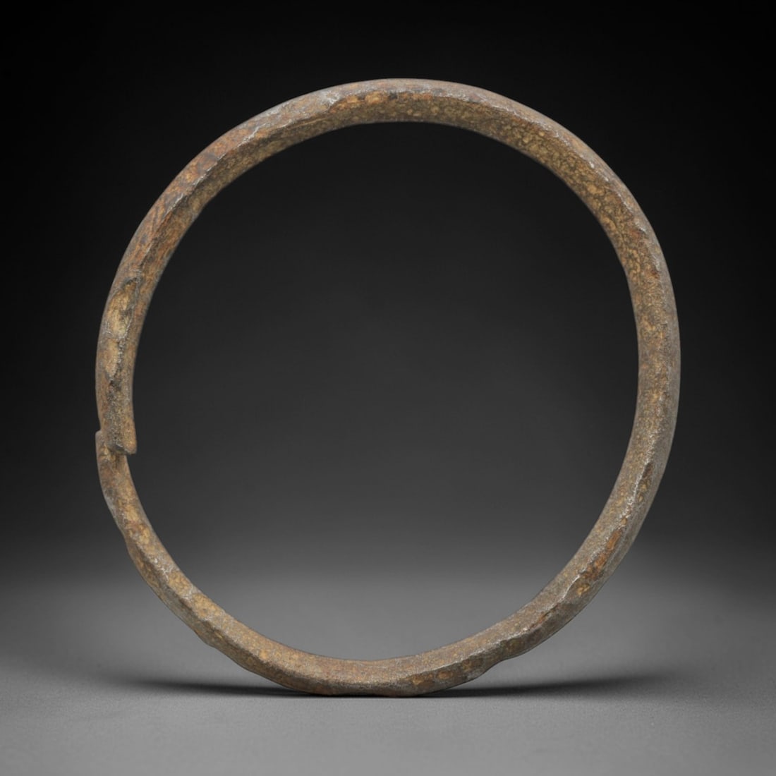 A Celtic Iron Bracelet, 2nd Century BCE - 1st Century CE, 8FV: Forged from iron with a flattened, slightly curved section, the bracelet is formed as a near-complete circle with a narrow terminal gap. The surface exhibits a thick, brownish patina with extensive co