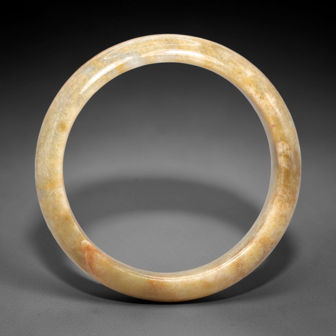 A Burmese Jadeite Jade Bangle, 20th Century, 5FS: A Burmese jadeite jade bangle, with a pale yellowish matrix and scattered russet-brown mineral inclusions. The bangle is of circular form, with a smooth, polished surface revealing the internal crysta
