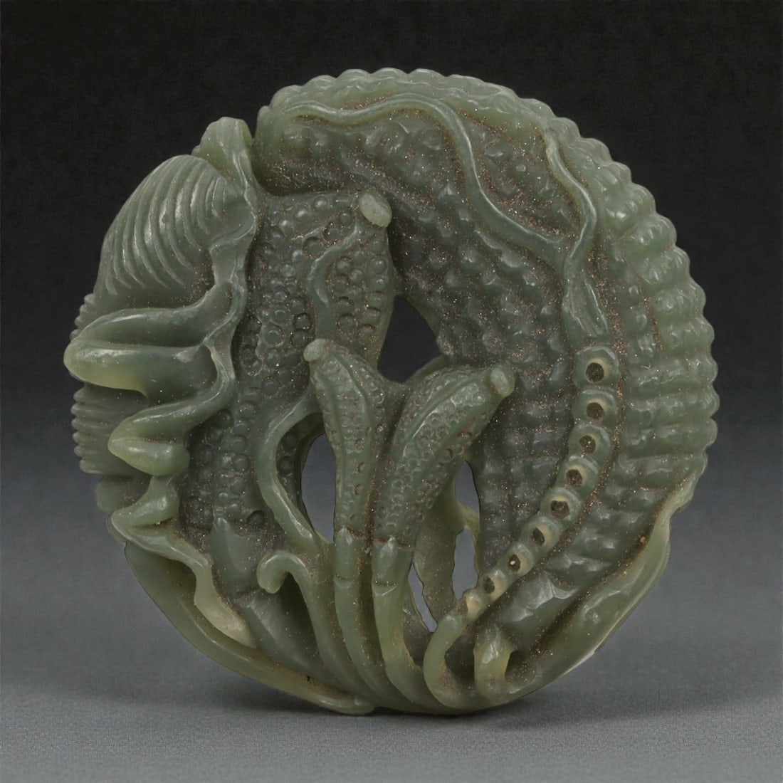 A Chinese Jade Fruit and Flower Openwork Disc, 20th Century, 46YA: Carved from dark green jade with lighter tonal variation and areas of soft translucency, the object is formed as a circular disc with extensive openwork carving. The composition is centered on a styli