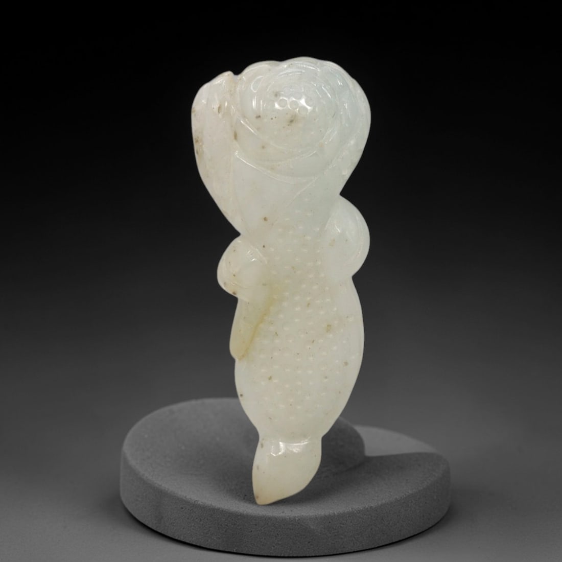 A Chinese Jadeite Jade Lotus-Form Pendant, 20th Century, 20FR: Carved from predominantly white jadeite jade with subtle internal veining and scattered dark inclusions, the pendant is formed as a stylized lotus stem and bud. The surface is executed in low relief,