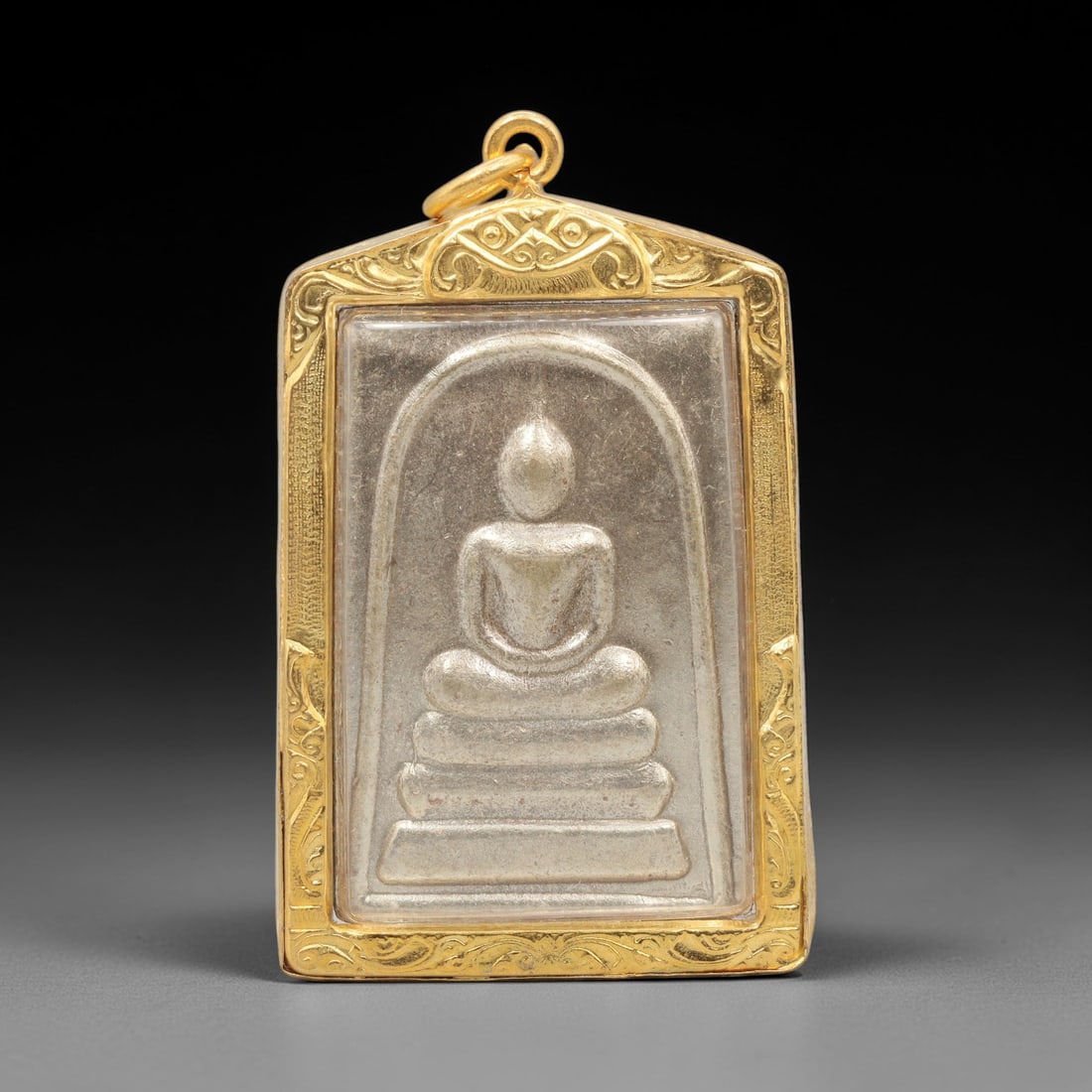A Thai Silver Phra Somdej Amulet in Gold Frame, Late 20th Century, 6FR: A rectangular silver amulet, measuring 6 x 3.5 cm, set within an ornate gold frame with a suspension loop at the apex. The obverse features the iconic Phra Somdej Buddha figure in seated meditative po