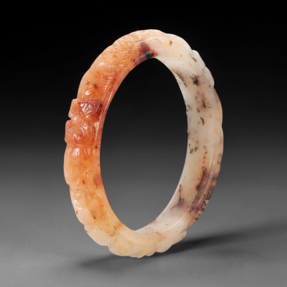 A Chinese Carved Jadeite Jade Bangle Bracelet, 20th Century, 35ZL: A fine jadeite bangle of flattened circular form, masterfully carved in relief with a continuous band of scrolling foliate and floral motifs. The stone exhibits a striking variegated palette, with a t