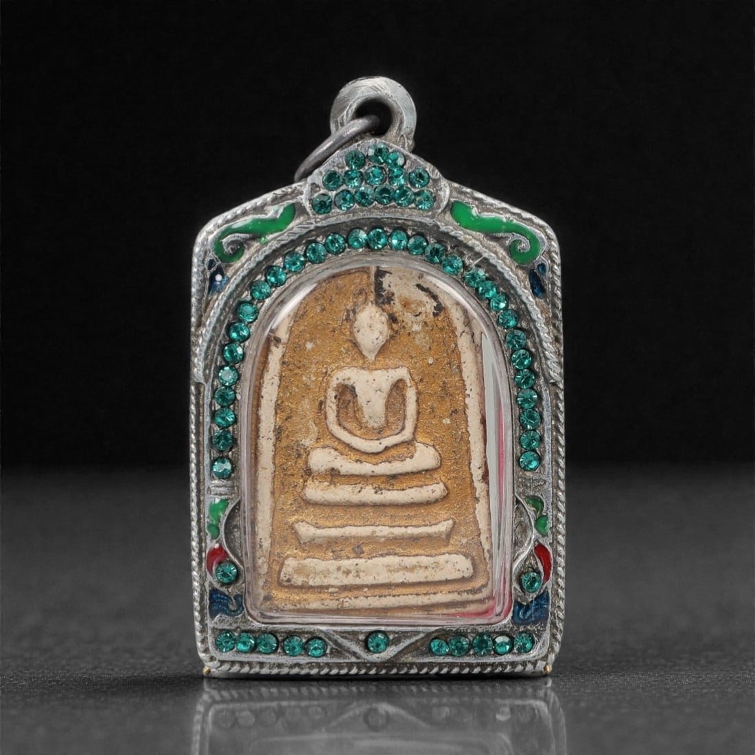 A Thai Buddha Amulet with Silver Frame, 20th Century, 41FP: The amulet is of rectangular form with a pointed upper edge. The obverse features a molded seated Buddha figure in meditative pose (dhyana mudra), rendered in a light-colored material against a tan gr