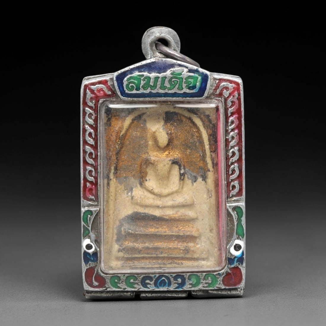 A Thai Phra Somdet Clay Amulet in a Polychrome Enamel Silver-Tone Case, 20th Century, 11ZK: This rectangular Phra Somdet amulet is crafted from sacred beige clay and encased in an ornate silver-tone metal case with a suspension loop at the apex. The obverse of the case is elaborately decorat