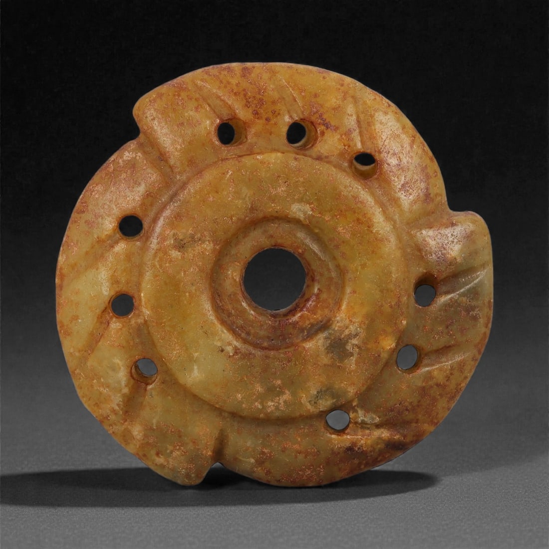 A Chinese Russet-Stained Nephrite Jade Disc Ornament, 20th Century, 45FD: Carved from pale green to yellowish nephrite jade with extensive natural russet and iron-rich staining across the surface. The object is circular in form with a raised central boss pierced by a circul