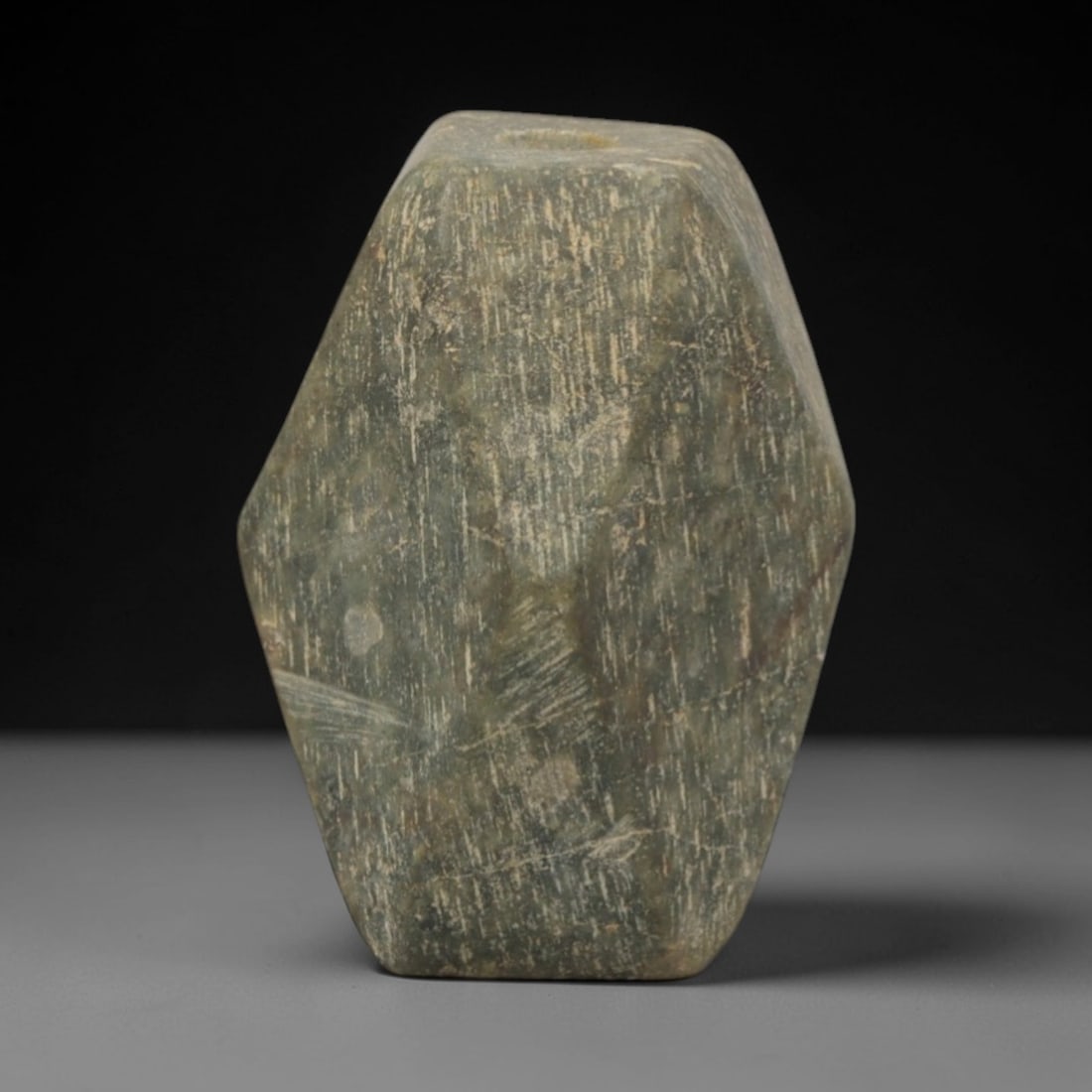 Ancient Green Stone Amulet - Near Eastern Hexagonal Pendant, 68XP: Carved from a mottled green stone, this amulet features a compact hexagonal form with a central perforation, designed for suspension as a wearable ritual relic. The craftsmanship is minimalist, emphas