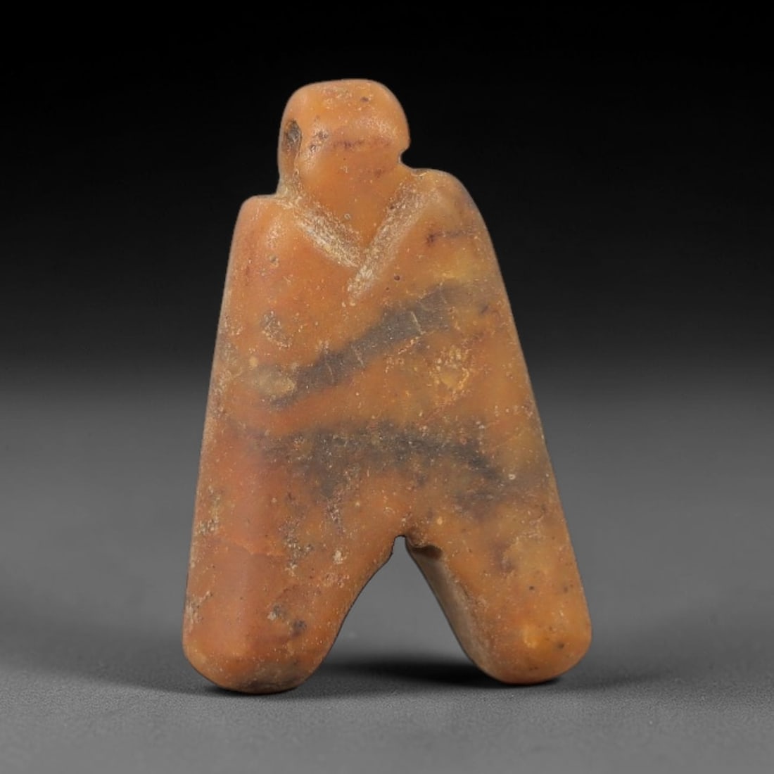 Ancient Stone Anthropomorphic Amulet - Near Eastern Ritual Figurine, 54AG: This amulet is carved from a single piece of warm amber-hued stone, exhibiting a fine-grained texture with subtle dark veining and natural mineral inclusions across its surface. The form is a stylized
