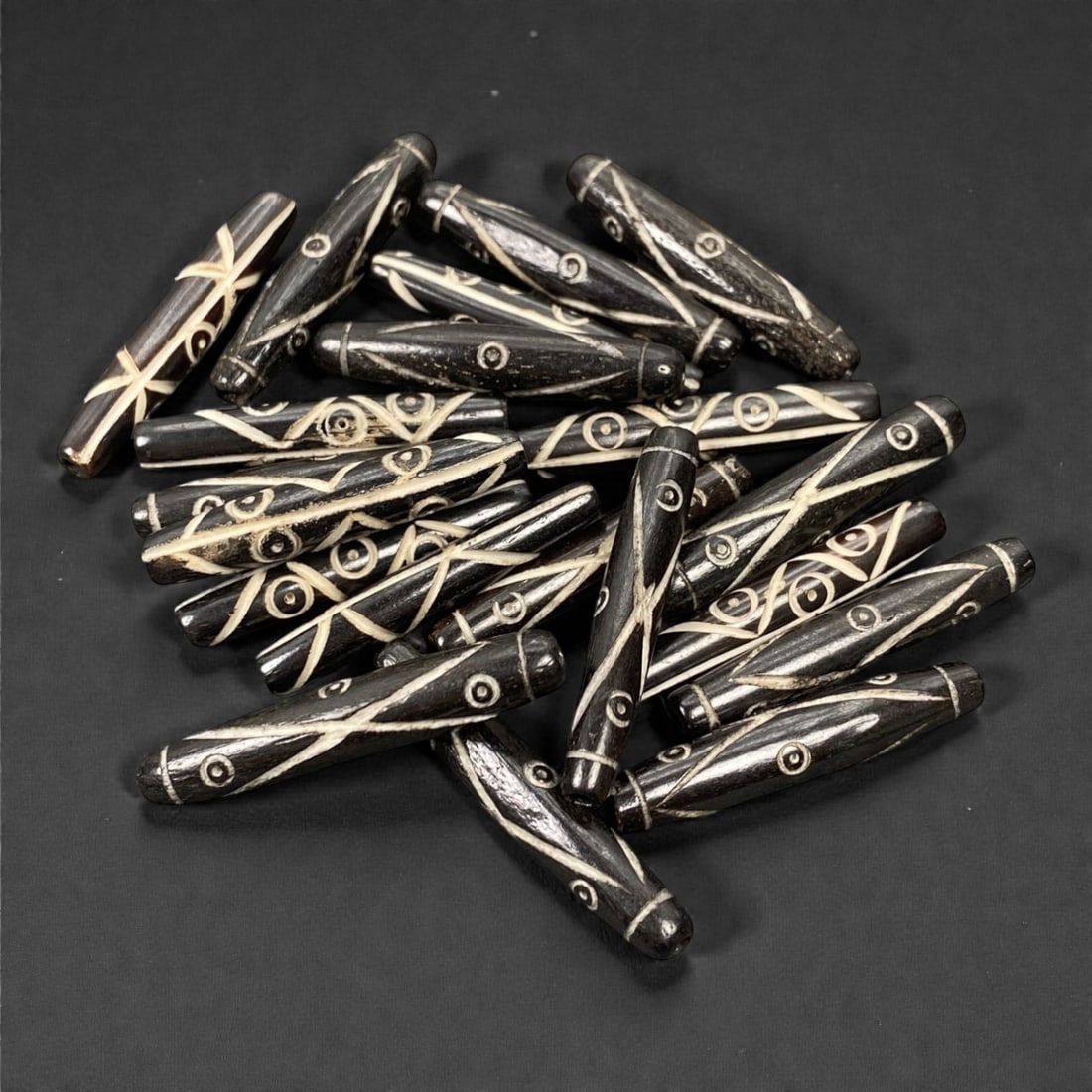 A Tibetan Bone Bead Group, Inlaid Linear and Circumferential Pattern, 20th Century, 80S: Composed of animal bone, each bead features an elongated cylindrical form with consistent proportions across the group. The surface displays an inlaid decorative scheme combining linear motifs and cir