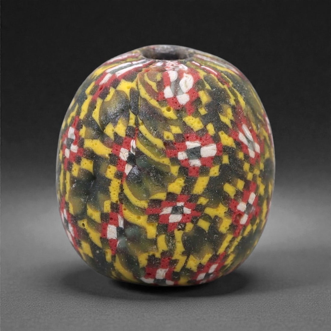 Ancient Glass Bead - Viking Mosaic Cane Sphere, 15Z: This spherical glass bead is formed from a dark glass body densely inlaid with mosaic cane fragments arranged in a complex checkerboard and lozenge pattern. The decoration features contrasting tones o