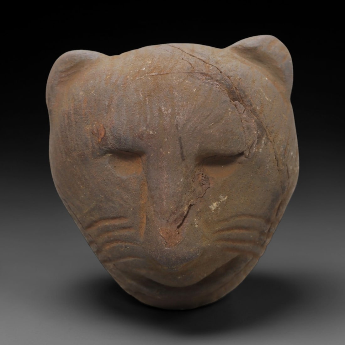 Ancient Stone Feline Head - African Maskette Figurine, 84FW: Carved from a coarse, textured stone, this African feline head maskette features a stylized feline visage with rounded ears, recessed eye sockets, a defined nasal ridge, and incised linear details sug