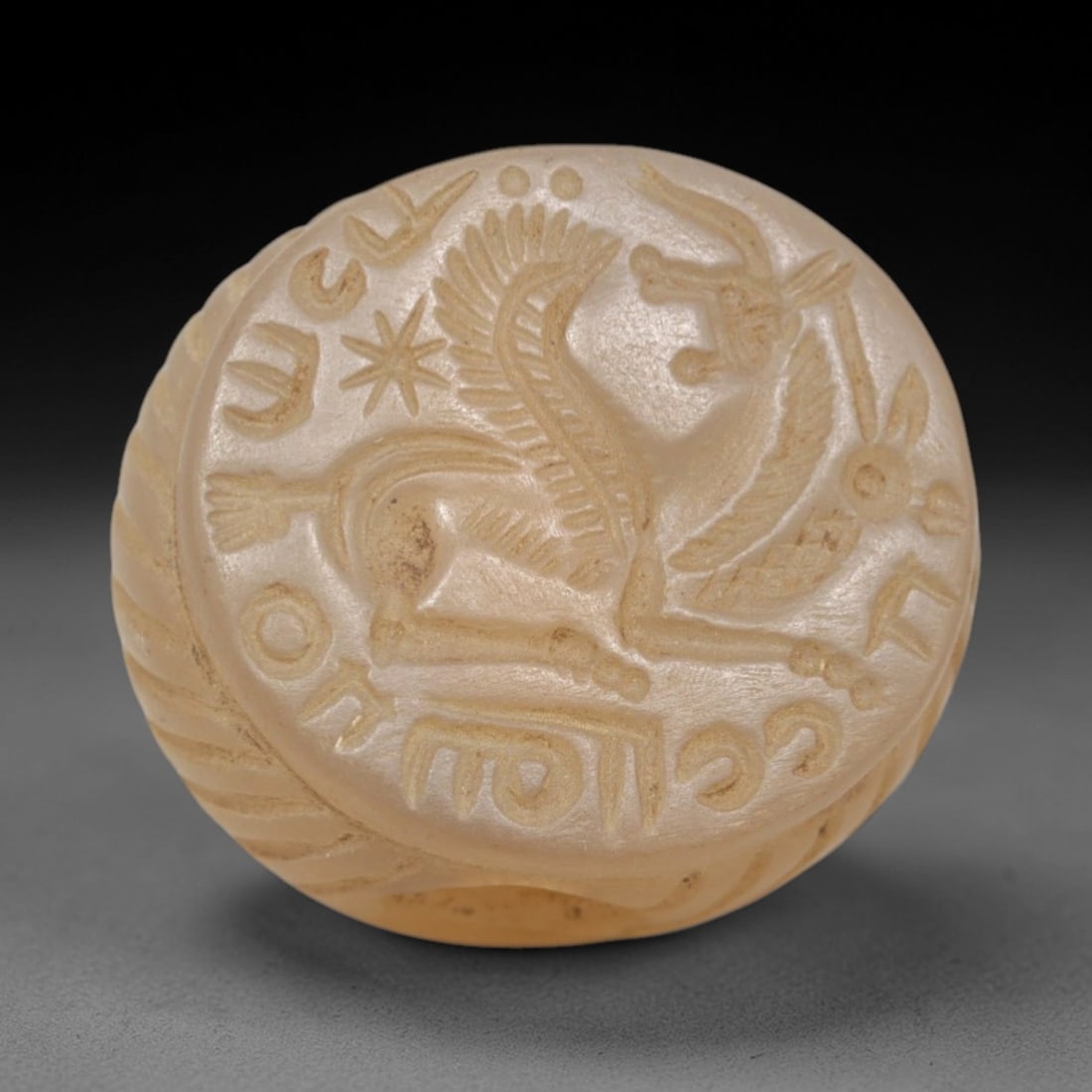 Ancient Chalcedony Hemispherical Stamp Seal - Near Eastern Griffin & Script, 43ZP: Crafted from translucent, pale chalcedony, this hemispherical stamp seal bears a deeply incised depiction of a stylized griffin, rendered in linear relief with detailed feathered wings, patterned tors