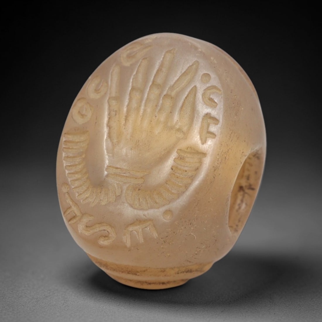 Ancient Chalcedony Hemispherical Stamp Seal - Near Eastern Hand Symbol & Script, 40ZP: Crafted from translucent, pale chalcedony, this hemispherical stamp seal bears a deeply incised depiction of a stylized hand symbol, rendered in linear relief with distinct finger segmentation and dec
