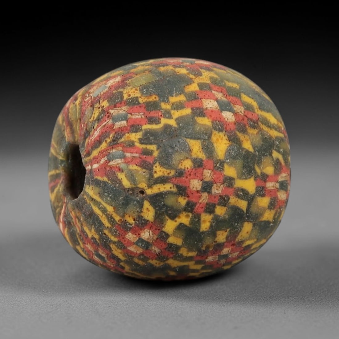 Ancient Glass Mosaic Bead - Roman Bead, 33ZM: This ancient bead is crafted from polychrome mosaic glass, formed using the millefiori technique characteristic of Roman glassworking traditions. The spherical form features a vibrant, irregular patte