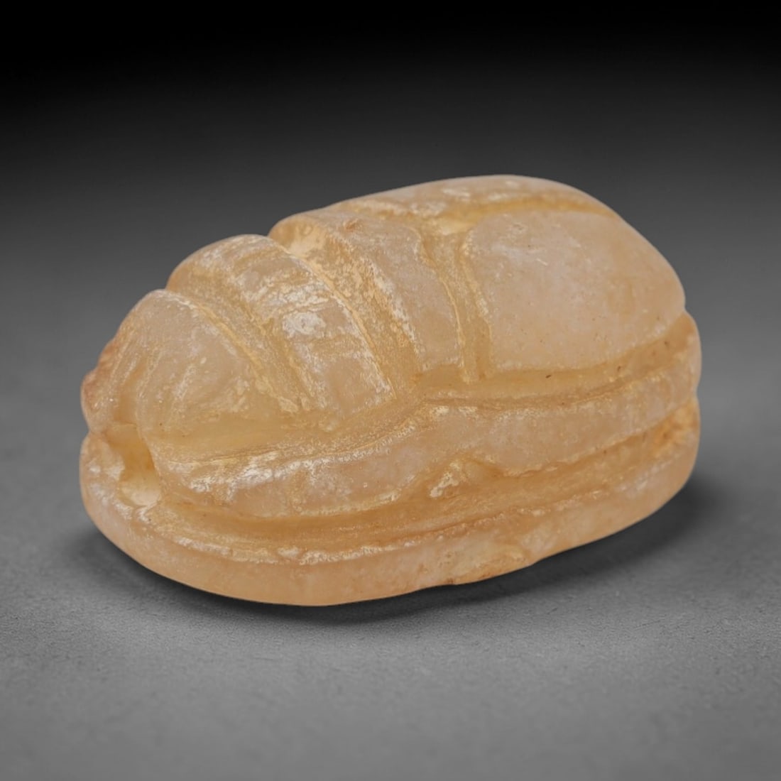 An Ancient Near Eastern Chalcedony Scarab Stamp Seal, 1st Millennium BCE, 11ZM: Carved from translucent chalcedony with a pale, milky patina and subtle internal veining, the object is formed as an oval scarab seal. The dorsal side is modeled in low relief with a segmented carapac
