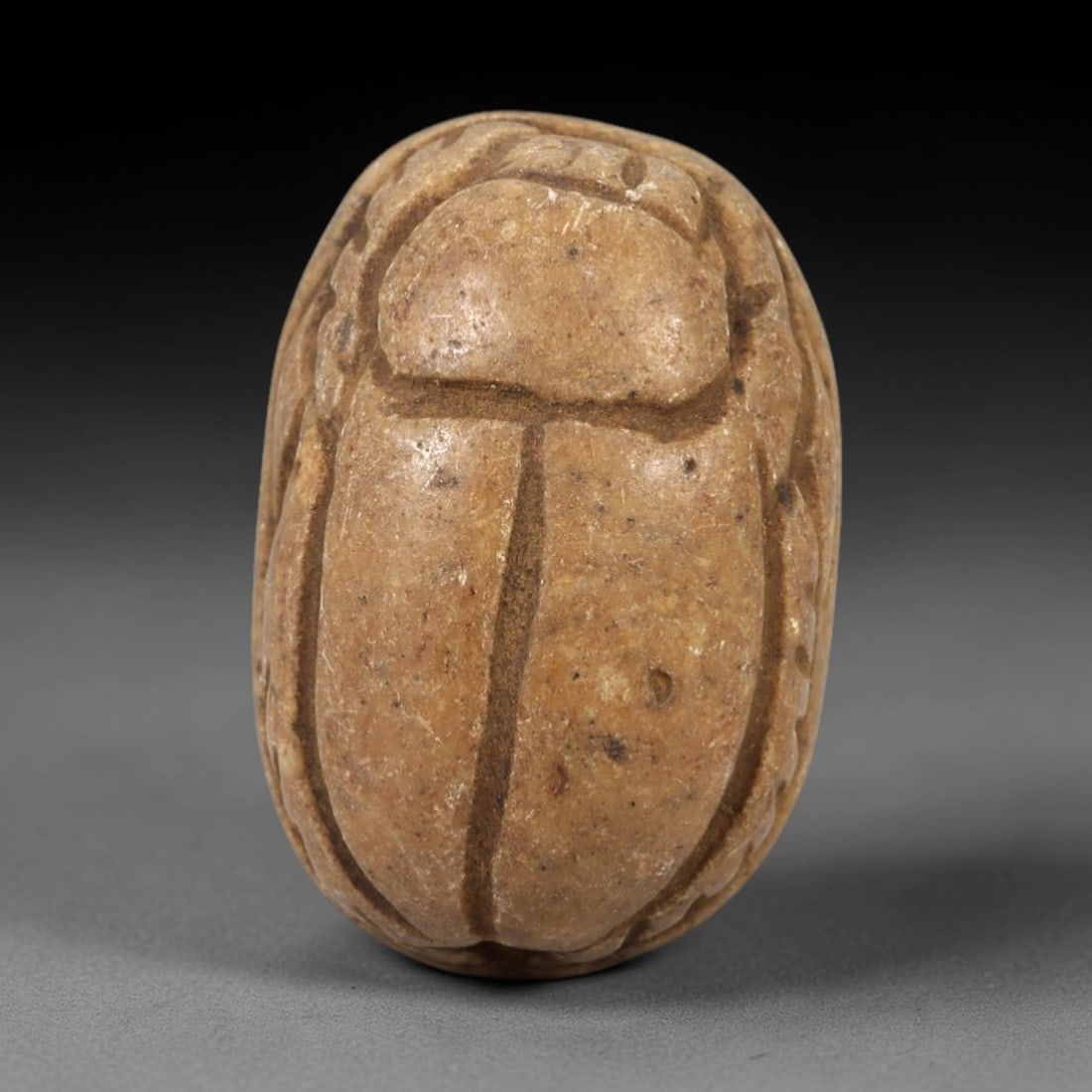 Ancient Egyptian Tan Stone Scarab - Amulet Figurine, 60AM: This artifact is a carved tan stone scarab amulet, crafted from a fine-grained, light brown stone with a smooth, polished surface and natural earthy patina. The dorsal side features simplified, bold l
