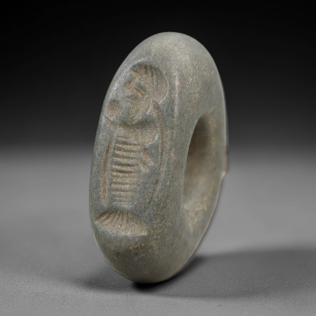 Ancient Stone Hemispherical Stamp Seal - Near Eastern Anthropomorphic Figure, 38AN: Carved from a dense, dark grey stone, this hemispherical stamp seal features a flat, circular face incised with a standing anthropomorphic figure. The figure is depicted with a prominent headdress, a