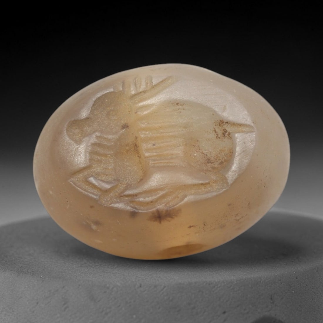 Ancient Chalcedony Stamp Seal - Near Eastern Antelope Figure, 59ZS: Crafted from translucent chalcedony, this oval stamp seal bears a deeply incised profile of a reclining antelope, rendered with linear detailing to define its horns, ribcage, and limbs. The iconograph