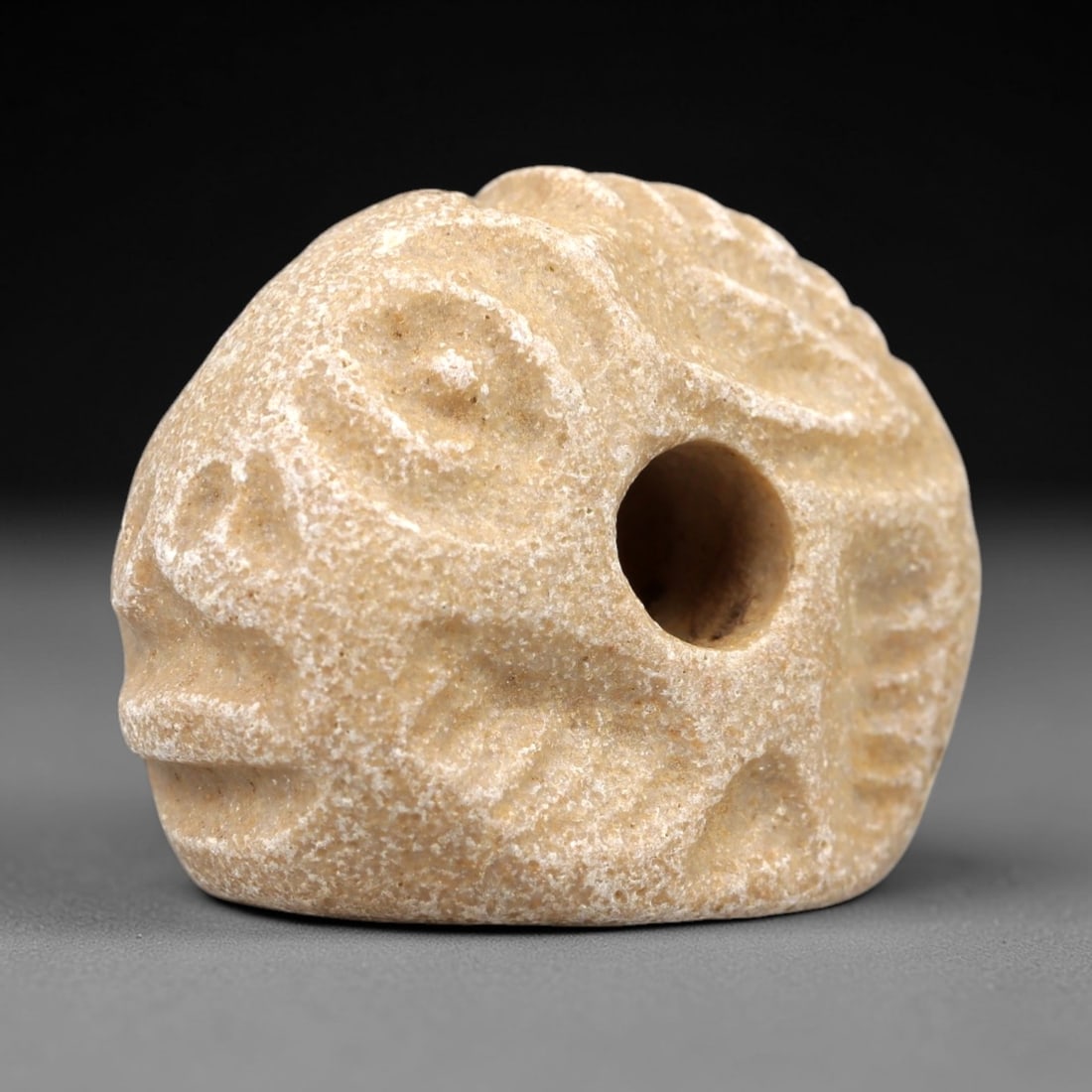 Ancient Limestone Humanoid Stamp Seal - Near Eastern Ritual Artifact, 1AN: Carved from soft limestone, this stamp seal features a stylized humanoid head form with distinct facial features, decorative linear patterns, and a central perforation for suspension. The pale limesto
