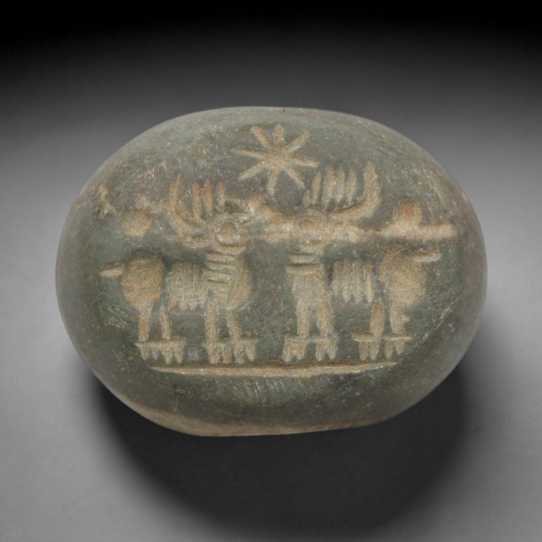 Ancient Stone Hemispherical Stamp Seal - Near Eastern Animal Procession Figure, 47ZS: Crafted from dense, greenish stone, this hemispherical stamp seal bears incised carving of a procession of stylized animal figures, likely bovids or ibexes, with segmented torsos, prominent horns, and