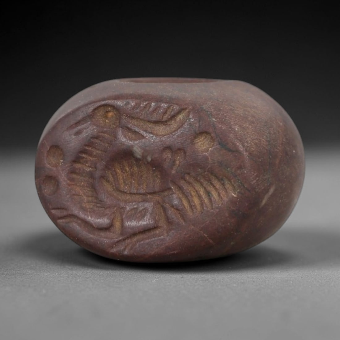 Ancient Stone Hemispherical Stamp Seal - Near Eastern Bird Figure, 89AN: Carved from a dense, dark reddish-brown stone, this hemispherical stamp seal features a flat, oval face incised with a stylized bird in profile. The bird is rendered with detailed linear patterns defi