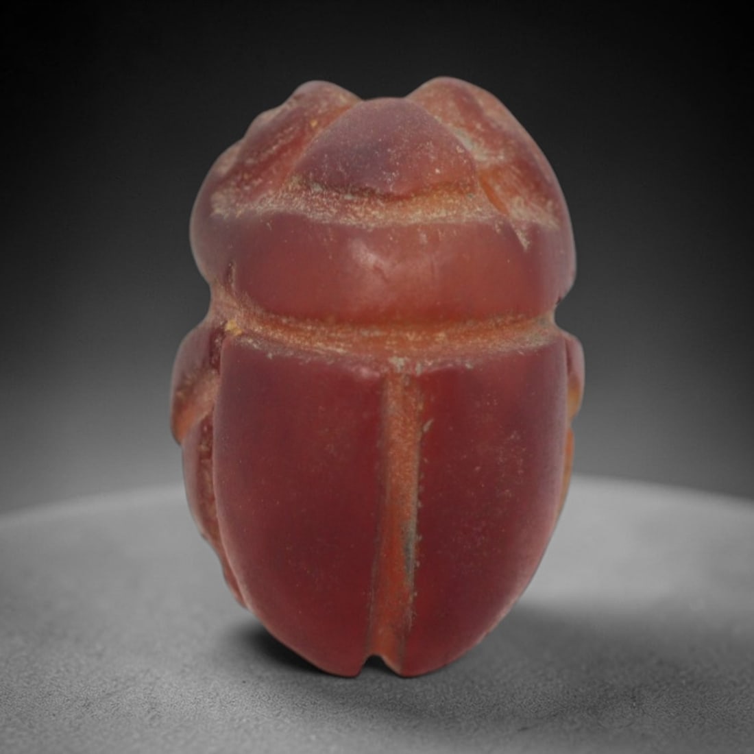 Ancient Egyptian Carnelian Scarab Amulet - Carved Bead Figure, 14ZV: This amulet is carved from a rich, translucent carnelian, featuring the iconic scarab beetle form. The piece displays a domed back with incised details defining the head, elytra, and segmented body, a