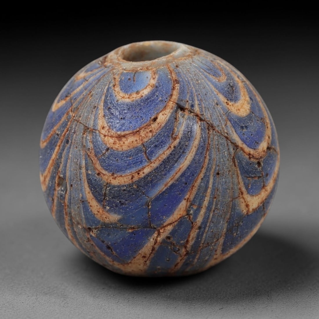 Ancient Islamic Glass Bead - Swirl Pattern Amulet Bead, 18FW: This spherical bead is crafted from translucent blue glass, adorned with flowing white swirl patterns that traverse its surface, accented by subtle earthy-toned inlays along the lines of the design. A