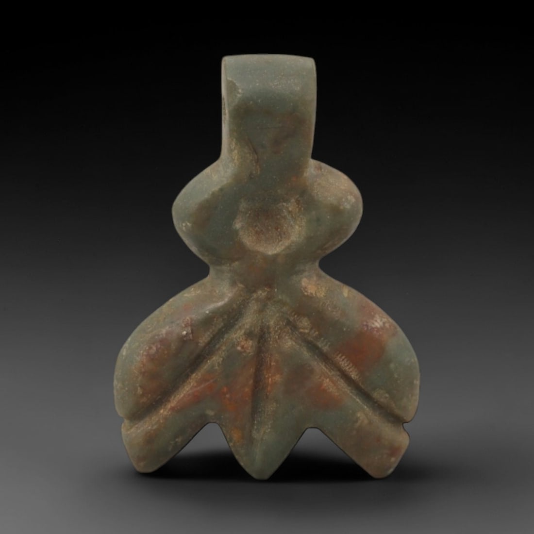 Ancient Stone Floral - Near Eastern Amulet Pendant, 38XR: Carved from muted green stone with reddish mineral inclusions, this amulet features a stylized floral form with a rectangular top suspension loop, bulbous central section, and lobed lower petals. The