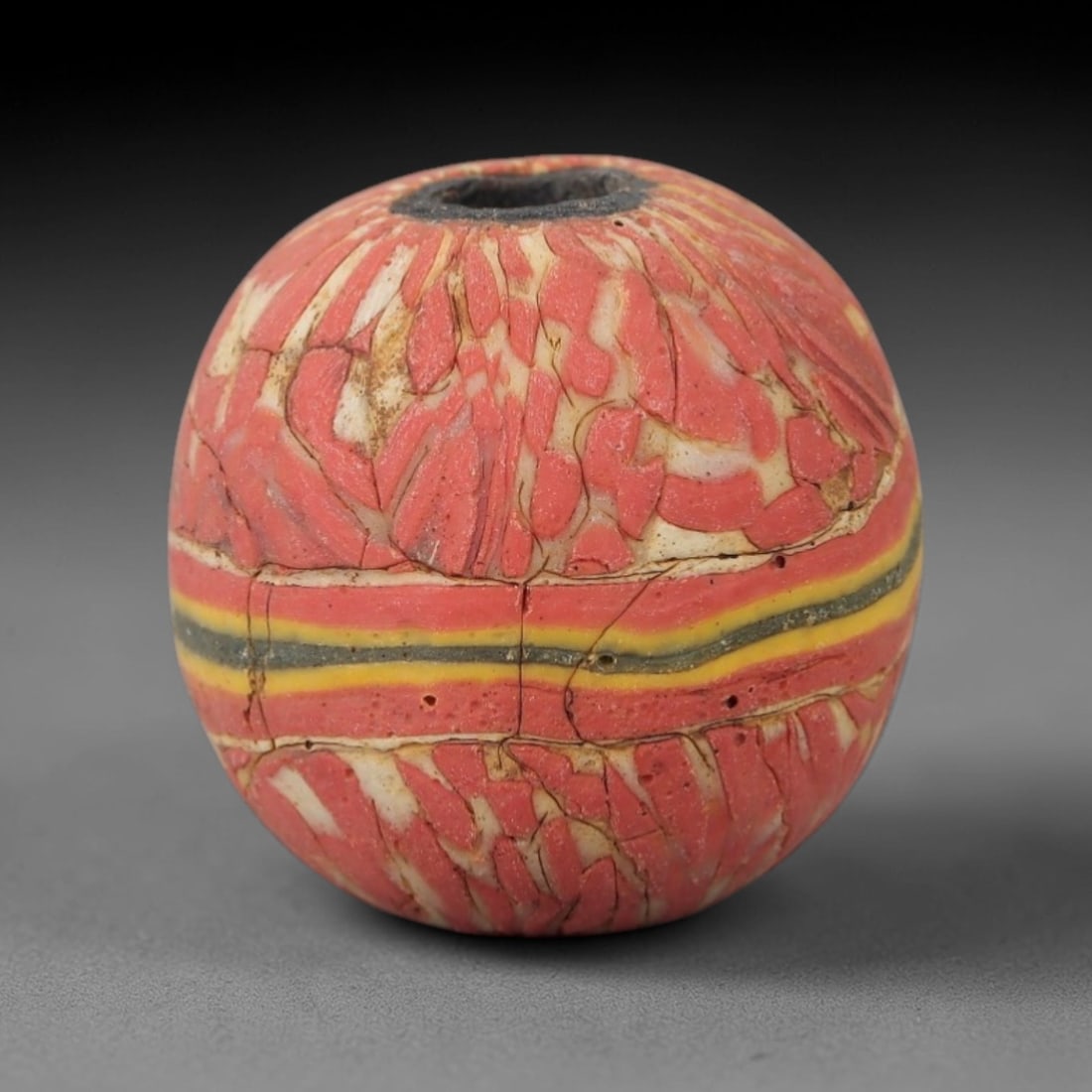 Ancient Glass Bead - Roman Striped Bead, 31ZM: This ancient bead is crafted from polychrome glass, formed using mosaic and trailed decorative techniques characteristic of Roman glassworking traditions. The spherical form features a dominant red ma