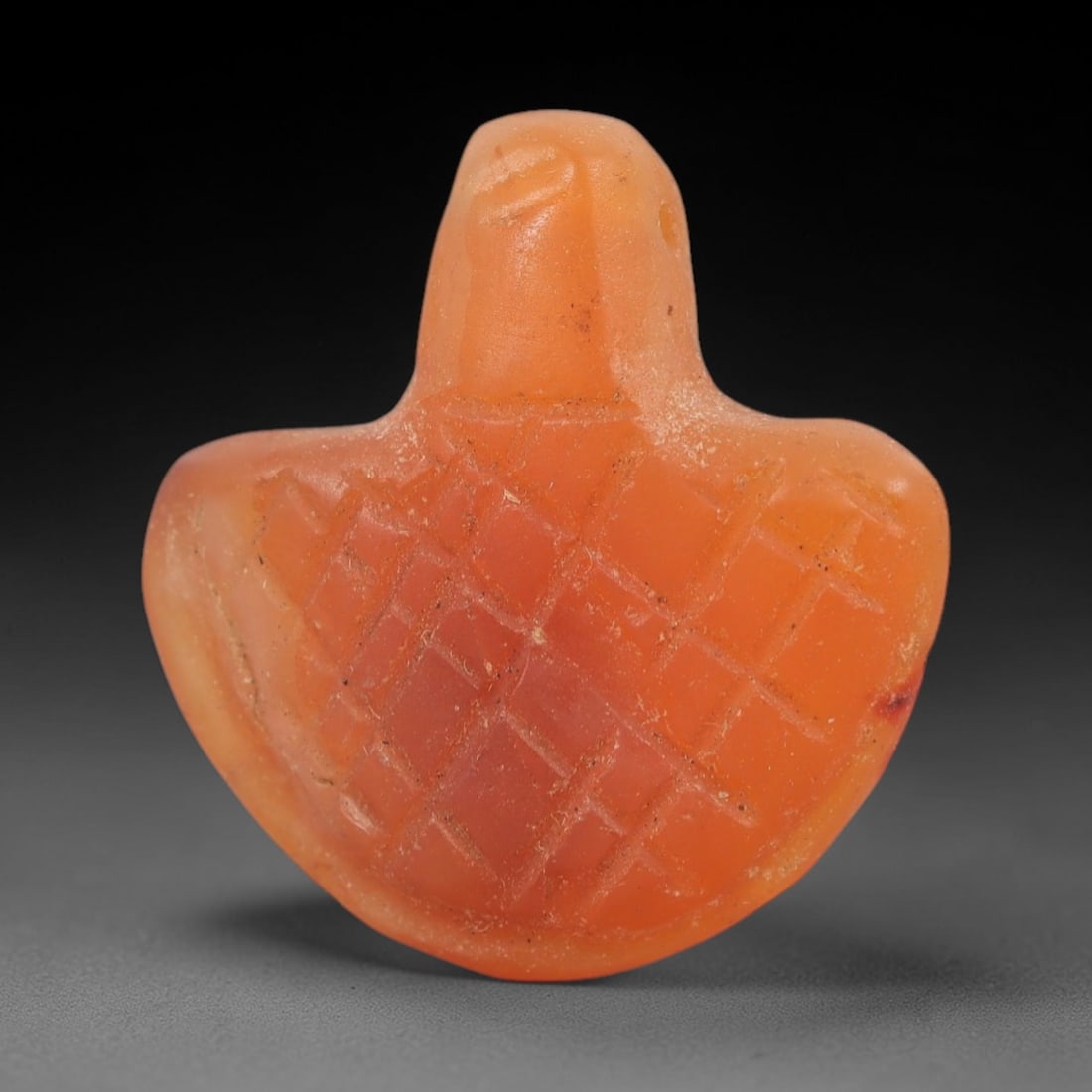 Ancient Carnelian Bird Amulet - Near Eastern Figurine, 68AJ: Carved from warm orange carnelian with natural reddish inclusions, this amulet is formed as a stylized bird with outstretched wings, featuring incised cross-hatching across the body to denote feather