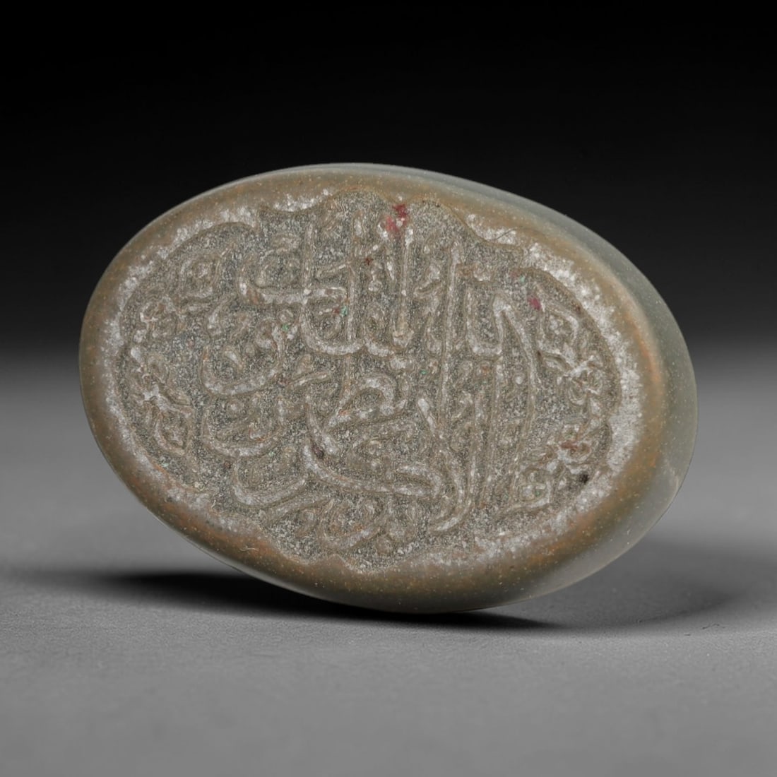 Ancient Islamic Calligraphic Seal Amulet - Middle Eastern Intaglio, 13AJ: Carved from smooth, muted green stone (likely serpentine or soapstone), this oval amulet is a functional seal featuring deeply incised Arabic calligraphy within a decorative foliate border, consistent