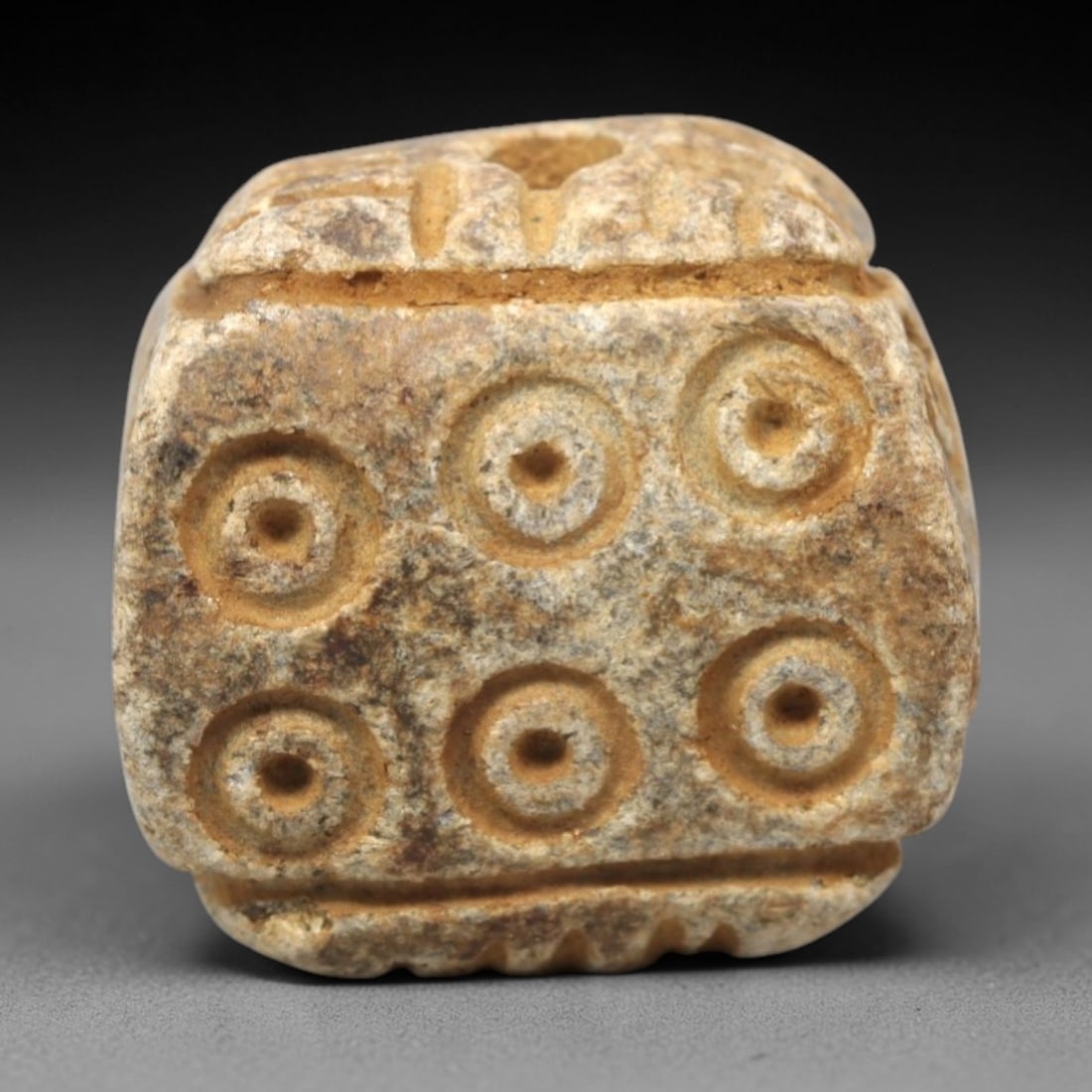 Ancient Steatite Amulet Bead - Near Eastern Concentric Circles, 21XV: Carved from granular steatite, this ancient amulet bead features a blocky, faceted form with a vertical suspension hole at the top, designed for wearable use. Its visible faces are decorated with a sy