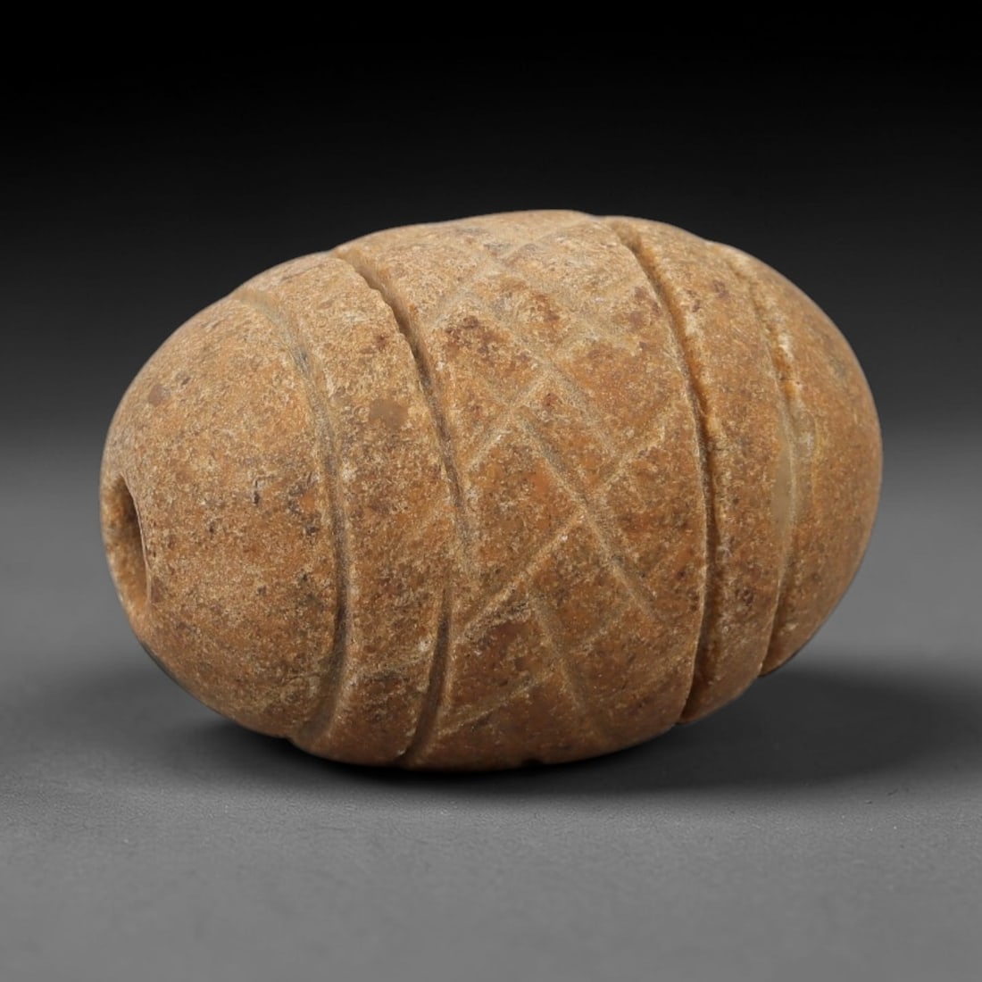 Ancient Egyptian Stone Bead - Parallel Line Carving, 72AE: Carved from stone, this ancient Egyptian bead features parallel linear patterns on its surface, a common decorative technique in Egyptian beadwork from the Late Period. The compact form has a central