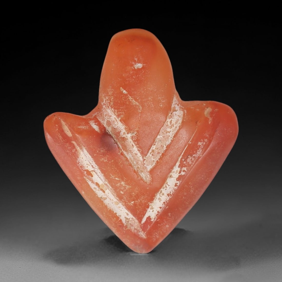 Ancient Carnelian Anthropomorphic Amulet - Near Eastern Figurine, 35AJ: Carved from rich orange-red carnelian, this amulet takes the form of a stylized anthropomorphic figure with broad, wing-like projections and a tapering lower body. The surface features prominent incis