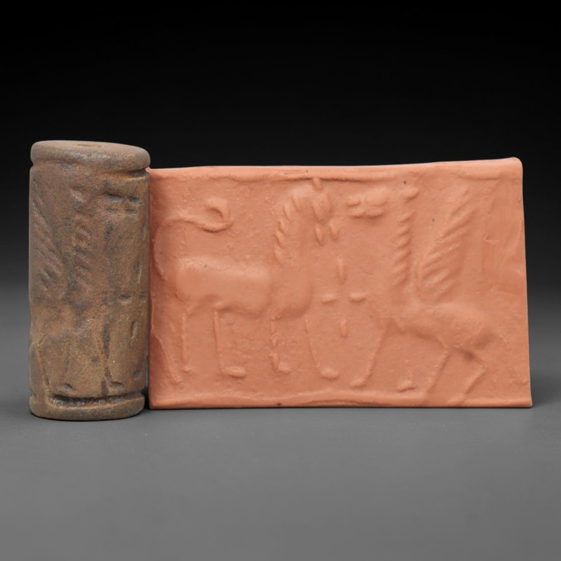Ancient Steatite Cylinder Seal - Mesopotamian Winged Creature Scene, 33AL: Carved from weathered, earthy steatite, this ancient Mesopotamian cylinder seal depicts a stylized confrontation scene, executed with the characteristic glyptic simplicity of Mesopotamian Bronze Age a