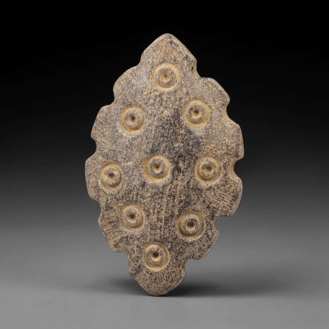 Ancient Steatite Amulet - Near Eastern Concentric Circles, 9AL: This amulet is carved from smooth steatite, shaped into an elongated, leaf-like form with a serrated upper edge and a rounded lower edge. The surface is decorated with multiple incised concentric circ